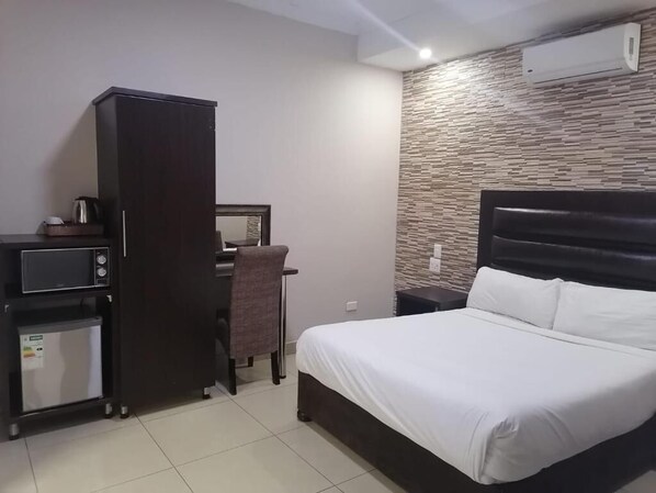 Habitación de hotel con cama, escritorio, silla, armario y un refrigerador pequeño.