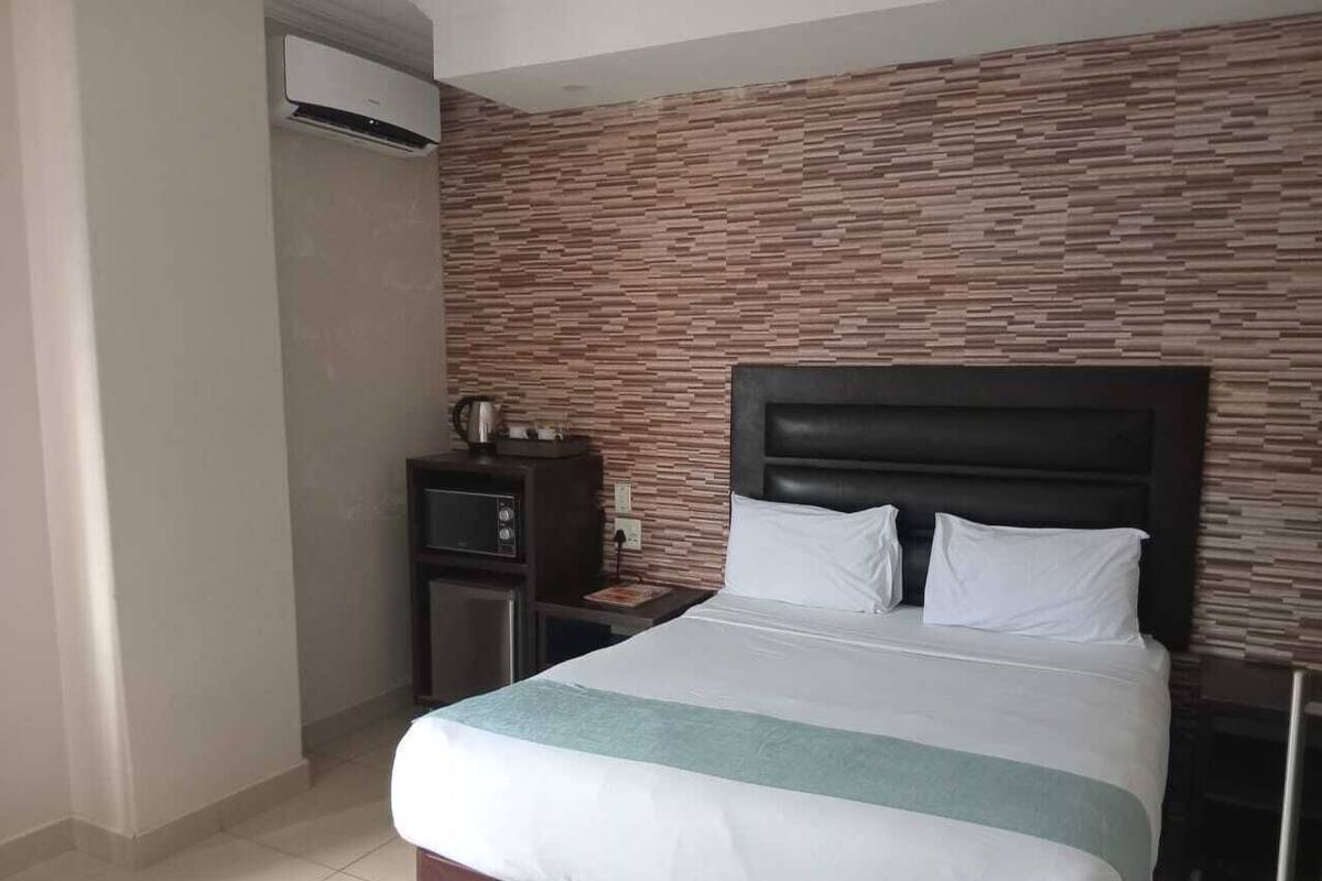 Een hotelkamer met een groot bed, een nachtkastje, een klein bureau en een airconditioner.