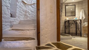 A bathroom with stone steps leading to a shower area, a sink with toiletries, and a mirror above the sink. - Anemomylos-Windmill (Syros)