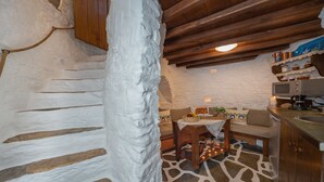 A rustic kitchen with a stone floor, wooden cabinets, and a wooden staircase. - Anemomylos-Windmill (Syros)