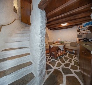 A rustic kitchen with a stone floor, wooden cabinets, and a wooden staircase.