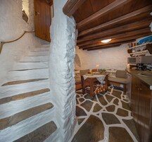A rustic kitchen with a stone floor, wooden cabinets, and a wooden staircase.