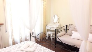 A bedroom with a bed, a bedside table, a mirror, and a window with curtains. - B&B Le Mi' Cocche (Capannori)