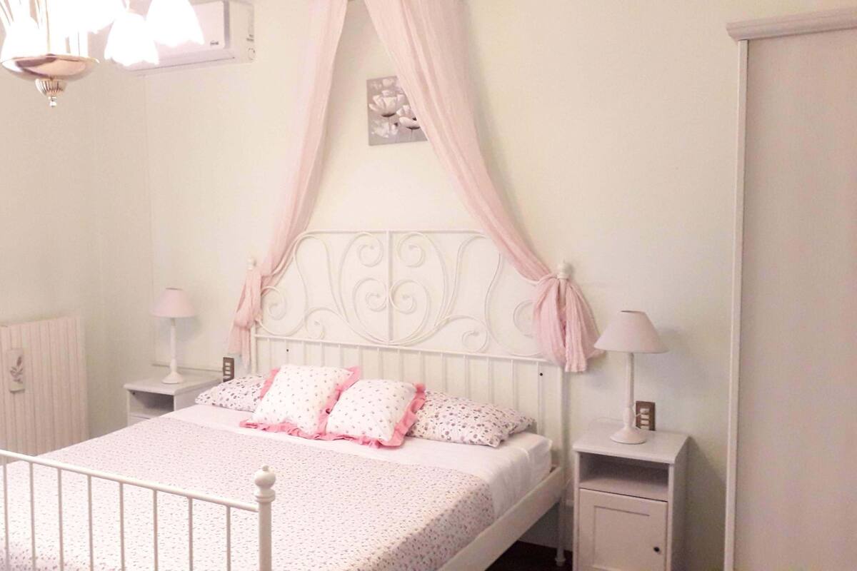 Un dormitorio con estructura de cama metálica blanca, dos mesitas de noche con lámparas y un radiador.
