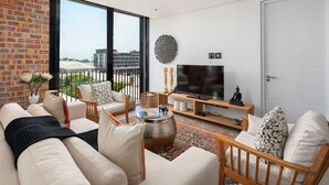 A modern living room with a large TV, comfortable seating, a coffee table, and a view of the city through large windows. - The Signature 401 (Cape Town)