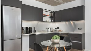 A modern kitchen with dark cabinetry, stainless steel appliances, and a glass dining table with chairs. - The Signature 401 (Cape Town)