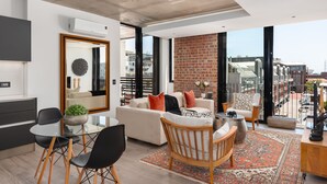 A modern living room with a sofa, chairs, a dining table, and a large window overlooking a cityscape. - The Signature 401 (Cape Town)