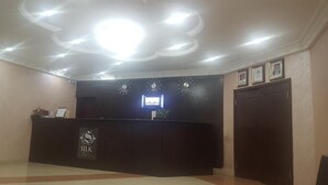 A reception area with a dark reception desk, a large circular light fixture on the ceiling, and framed pictures on the wall. - Silk Suites (Jos)