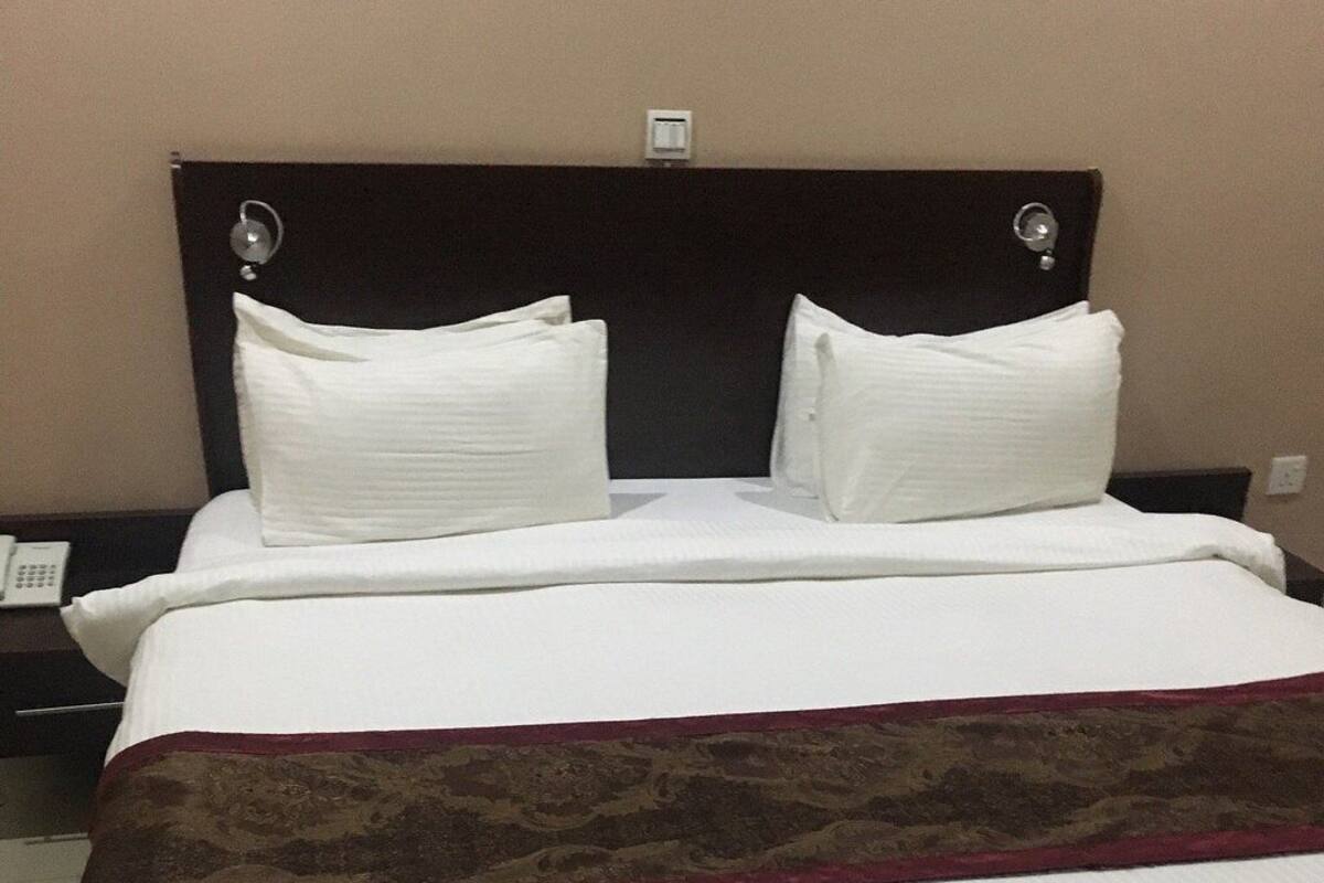 Une chambre d’hôtel avec un grand lit, deux oreillers blancs, une tête de lit sombre et un plaid décoratif rouge et marron.