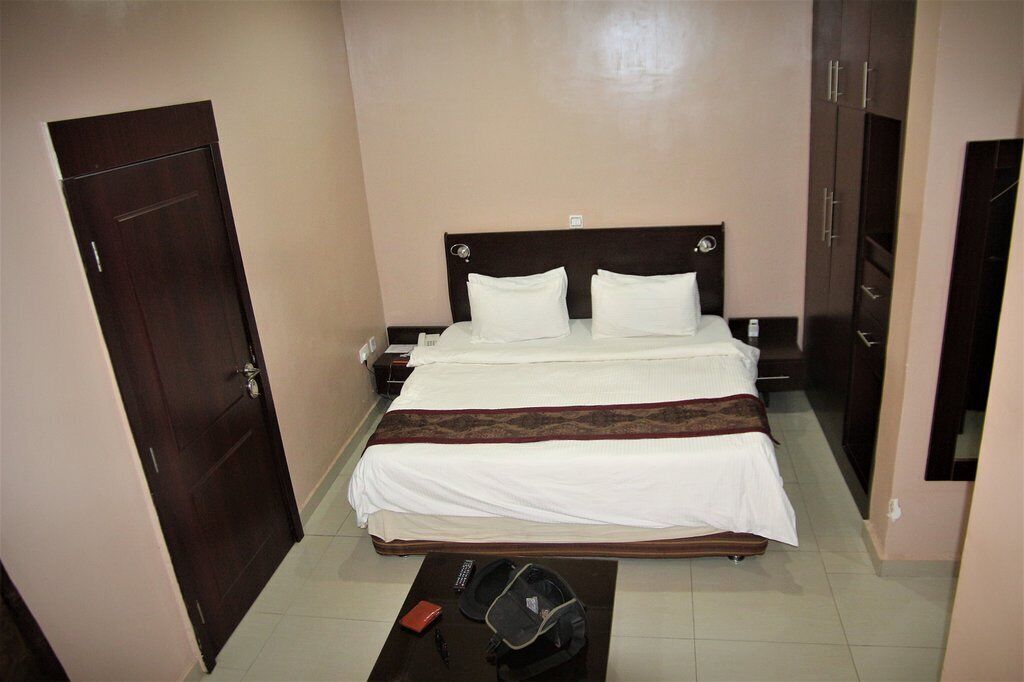 A hotel room with a bed, a desk, a chair, a wardrobe, and a door.