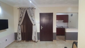 A room with a closed door, a flat-screen TV mounted on the wall, and a kitchen area with cabinets and a countertop. - Silk Suites (Jos)