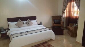 A neatly arranged bedroom with a large bed, two nightstands, a wooden chair, and a small table. - Silk Suites (Jos)