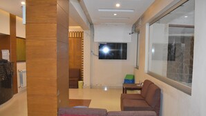 A modern living room with a flat-screen TV mounted on the wall, a wooden accent wall, and a seating area with two red chairs. - Hotel Akkas (Murree)