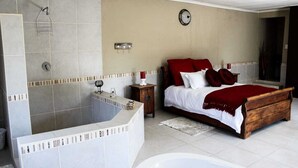 Un dormitorio con una bañera grande, una cama de madera con ropa de cama roja, una mesita de noche y un reloj de pared.