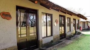Una hilera de habitaciones con ventanas y puertas amplias, techo de paja y un pequeño jardín.
