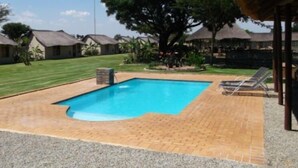 Una piscina con borde de ladrillo, rodeada por un césped y algunos árboles.