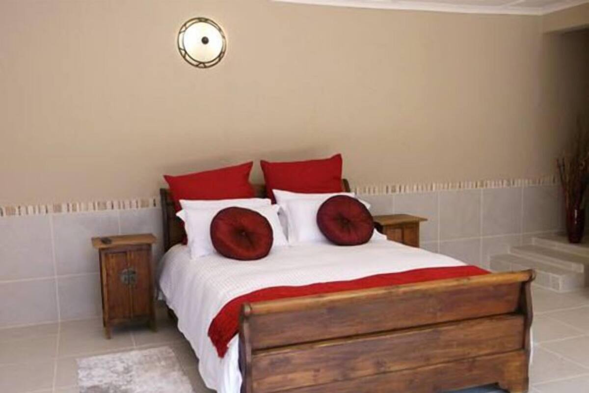 A bedroom with a wooden bed, red and white bedding, and a nightstand.