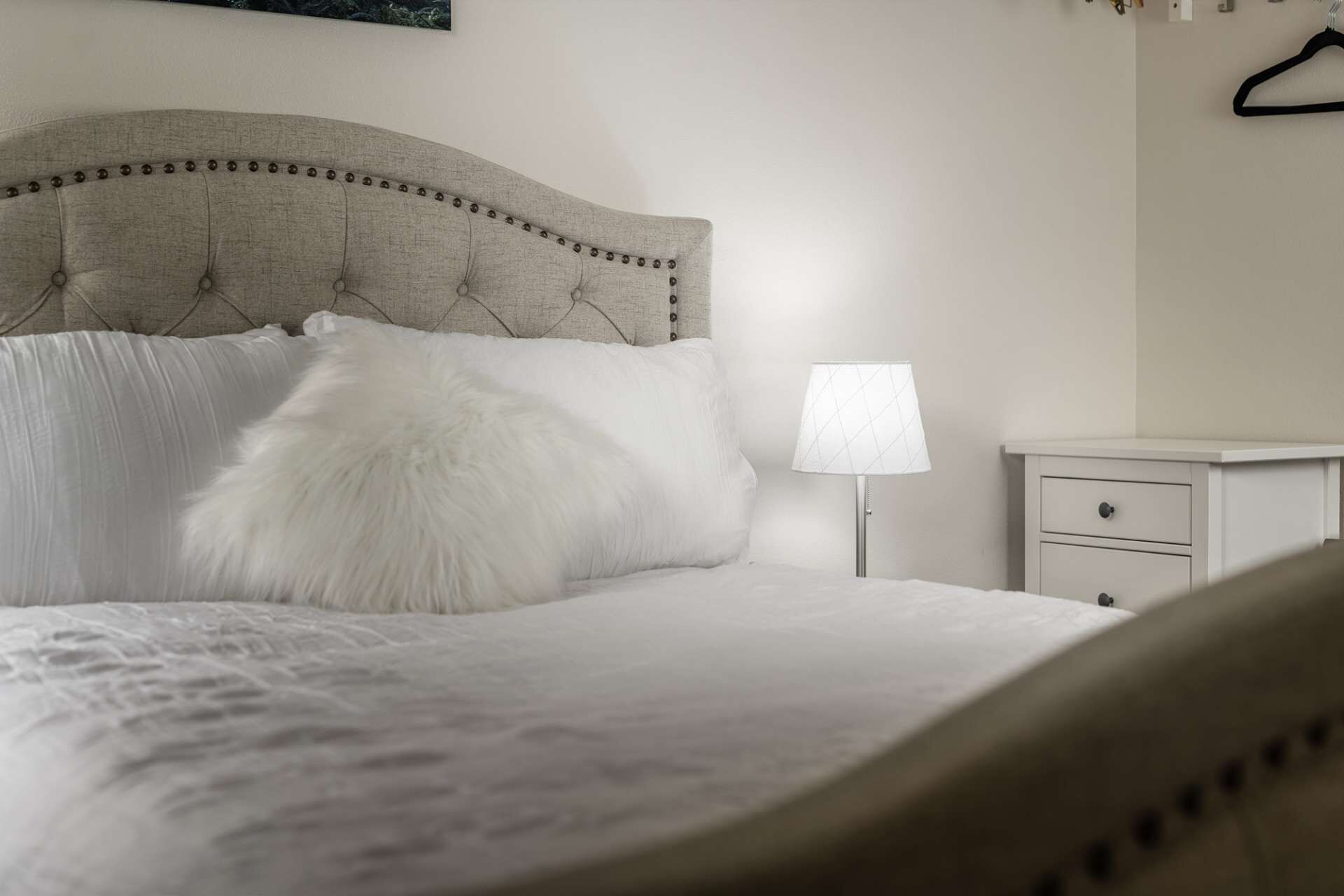 A neatly made bed with a tufted headboard, a fluffy pillow, and a bedside table with a lamp.