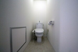 A small, narrow bathroom with a toilet, a hand dryer, and a paper towel dispenser.