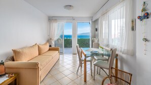 Ett modernt vardagsrum med en beige soffa, ett matbord i glas med stolar och utsikt över havet genom en glasdörr.