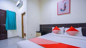 Ein Hotelzimmer mit einem Bett, einem Nachttisch, einer Wandklimaanlage, einer Tür und einem gerahmten Bild an der Wand.