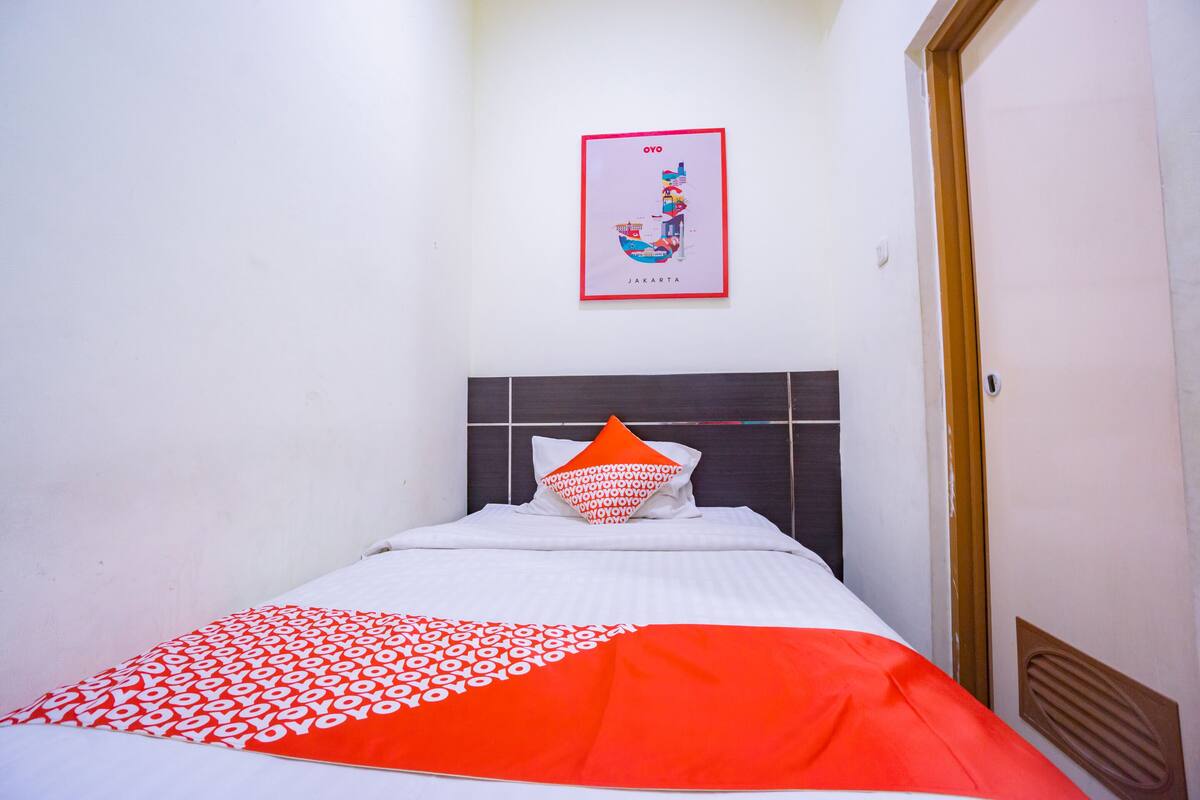 A neatly made bed with a patterned blanket, a pillow, and a framed map of Jakarta on the wall.