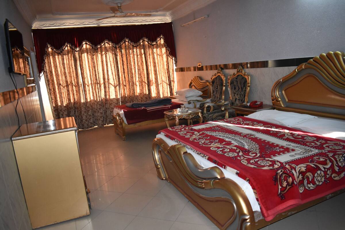 A hotel room with a large bed, a smaller bed, a vanity with a mirror, a desk, and a television.