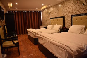 A hotel room with two beds, a chair, a desk, and a wall-mounted fan. - Hotel Faran Murree (Murree)