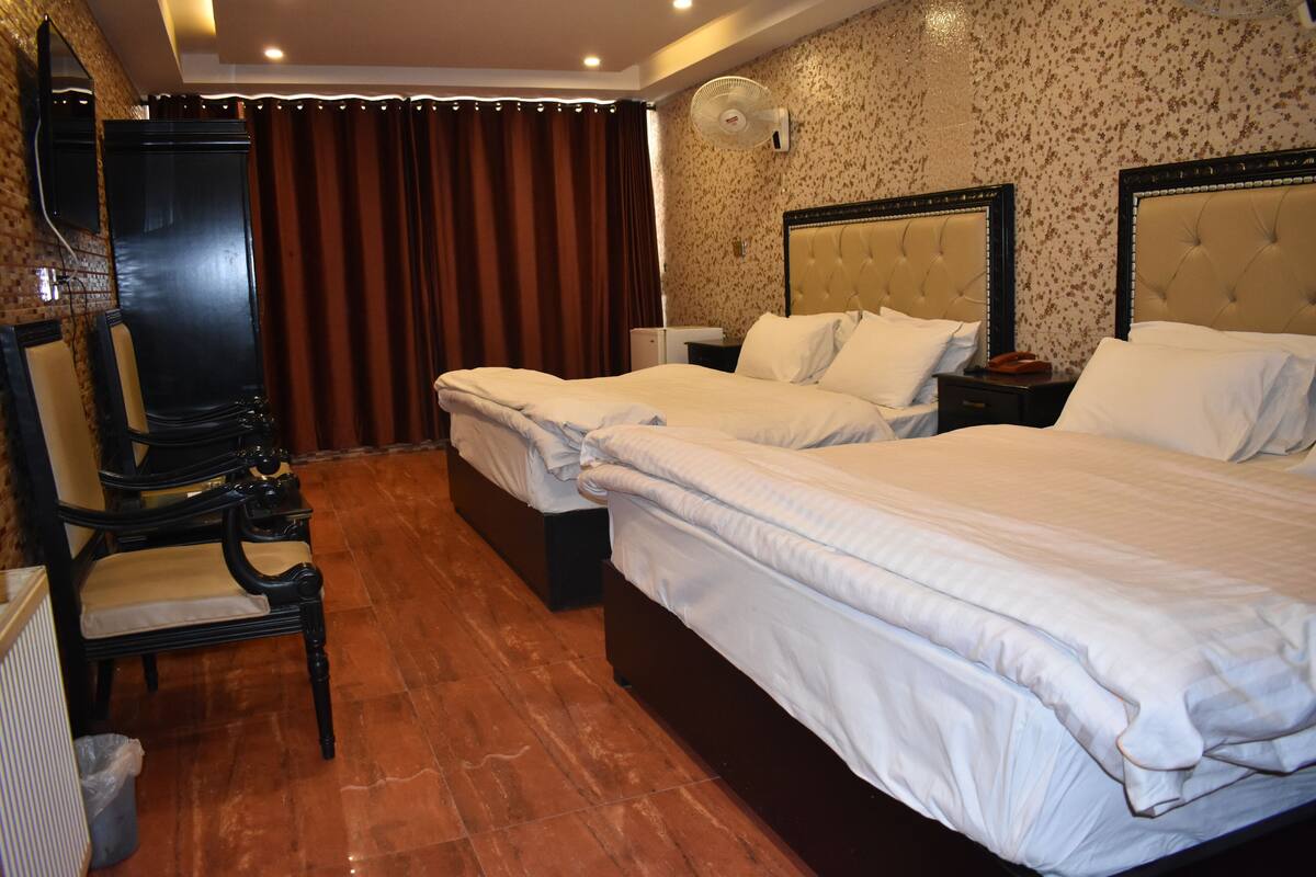 A hotel room with two beds, a desk, a chair, a mirror, a fan, and a curtain.
