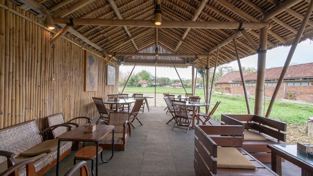 Un espace extérieur aménagé avec des sièges couverts, des murs, des tables et des chaises en bambou.