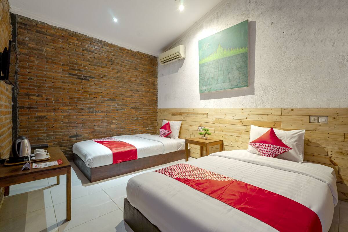 Une chambre d’hôtel avec deux lits, une tête de lit en bois, un mur en briques et un tableau accroché au mur.