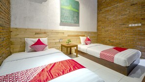 Une chambre d’hôtel avec deux lits, une tête de lit en bois, un mur en briques et un tableau accroché au mur.