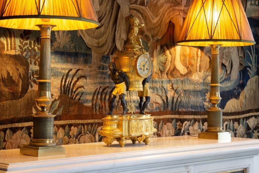 Une pièce décorée d’une tapisserie, d’une horloge et de deux lampes.