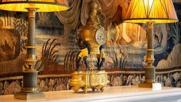 Une pièce décorée d’une tapisserie, d’une horloge et de deux lampes.