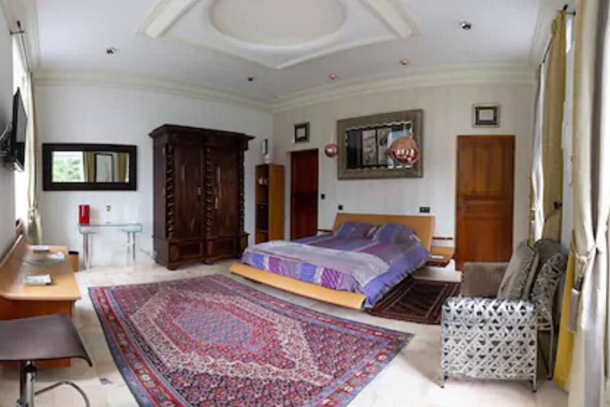 A bedroom with a large bed, a desk, a chair, a wardrobe, and a mirror.