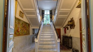 A grand staircase leading to a landing with a large painting on the left and a decorative headpiece on the right.