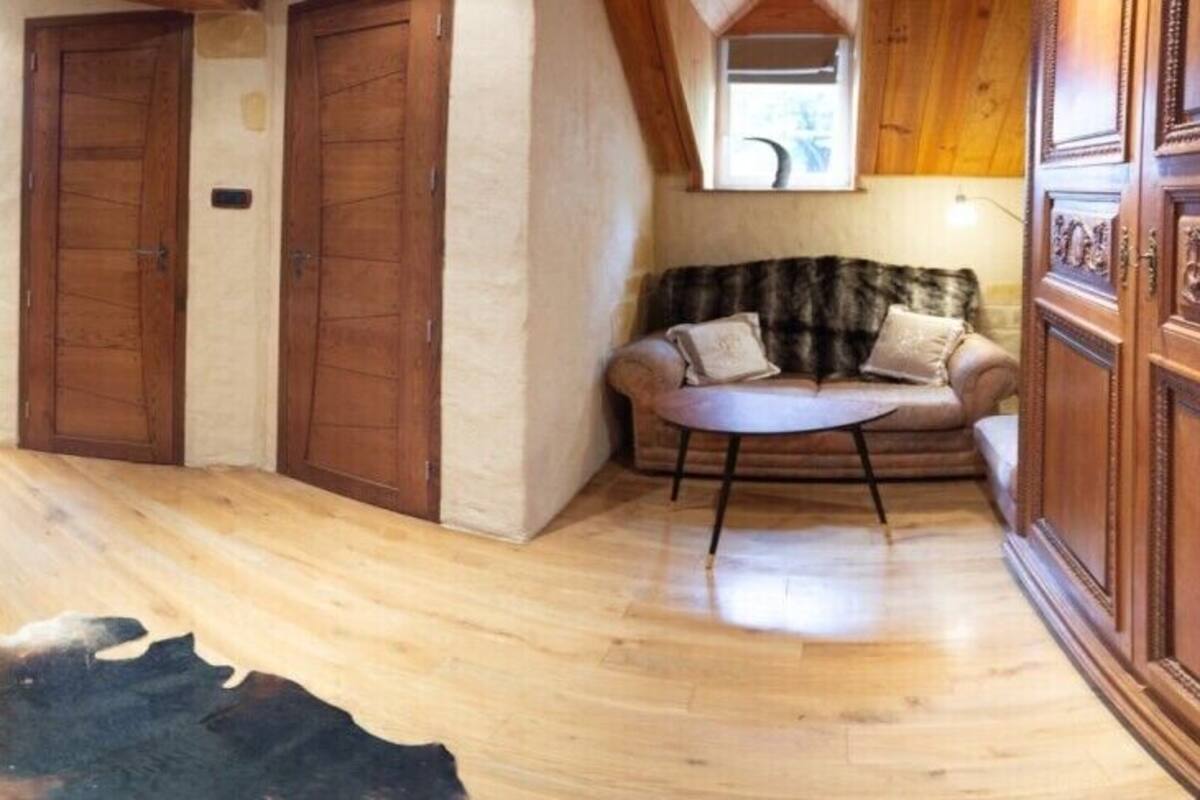 A cozy attic bedroom with a bed, wooden furniture, a television, and a stone wall.
