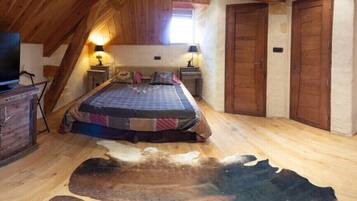 A cozy attic bedroom with a bed, wooden furniture, a television, and a stone wall.
