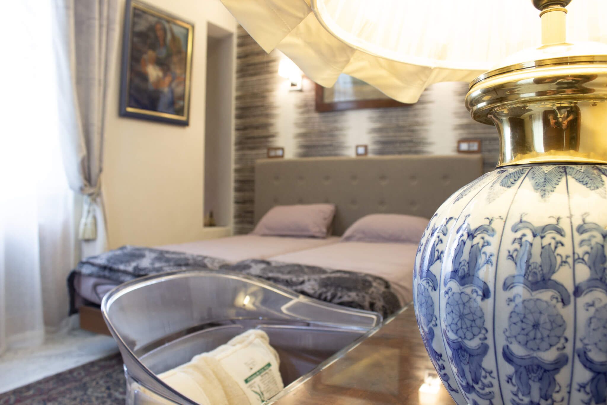 A hotel room with a bed, a bedside table with a lamp, and a decorative vase.