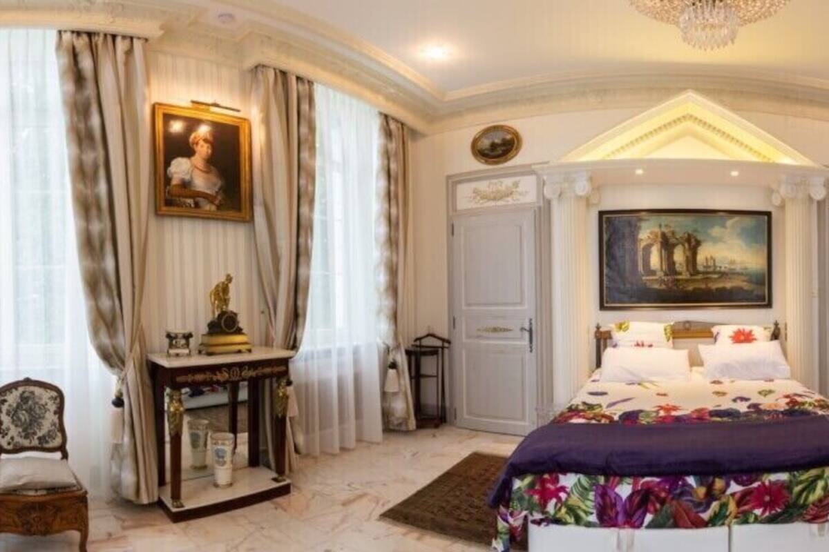 A spacious bedroom with a large bed, a desk, and a chair. There are two doors, one leading to a bathroom and another to a closet.