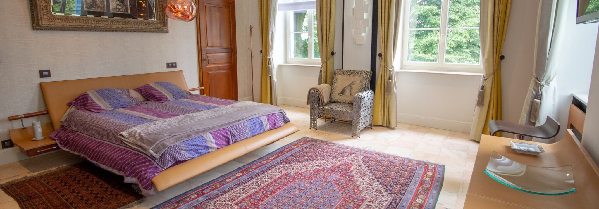 Un dormitorio con una cama grande, una silla, un escritorio y una ventana con cortinas.