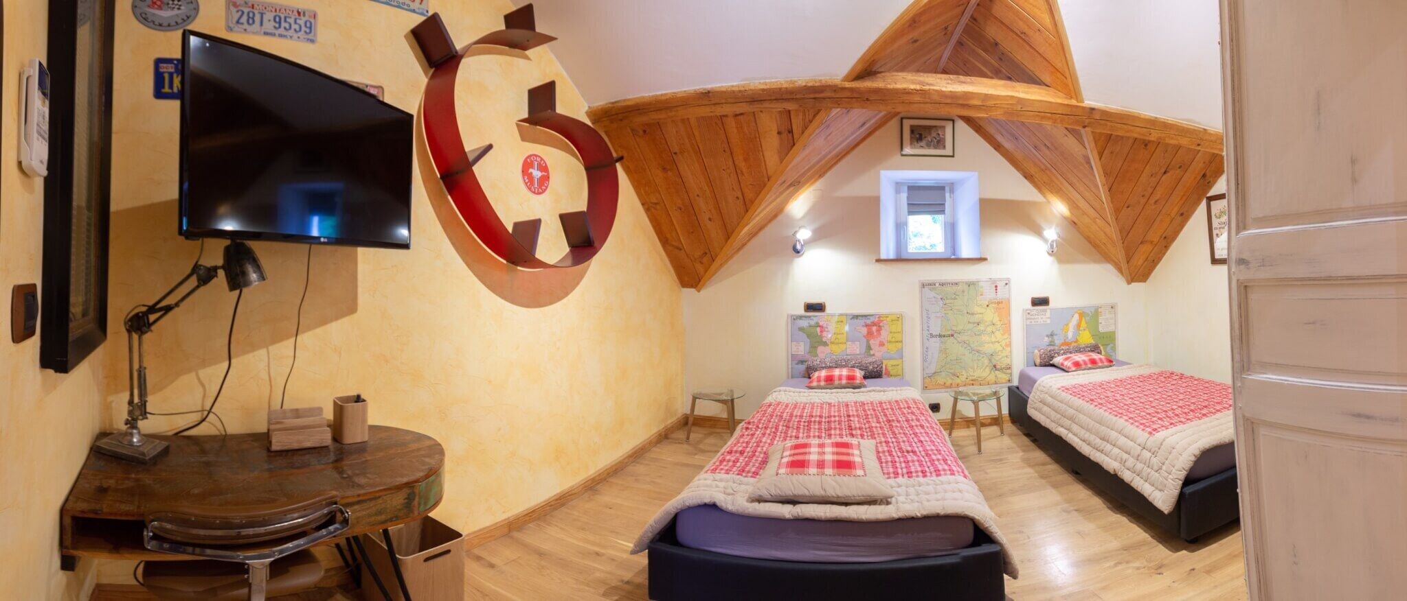 A room with two beds, a desk with a computer, a TV, and a large wall clock.