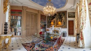 A luxurious room with a glass dining table, ornate chandelier, and a large painting on the wall.