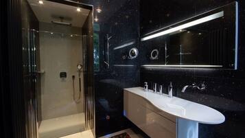 Un baño moderno con ducha envuelta en vidrio, un tocador amplio con lavamanos blanco y un diseño de pared oscuro con motivos estrellados.