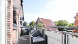 Un balcon doté de meubles en osier, d’une rambarde en métal et offrant une vue sur un bâtiment au toit rouge.