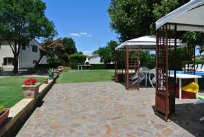 Relax in a serene outdoor space with a covered seating area, potted plants, and a gazebo for shade.