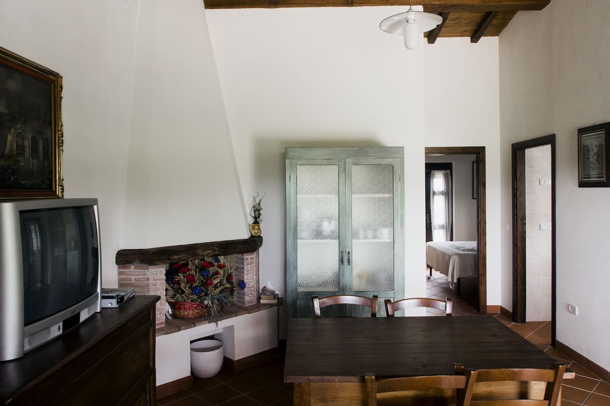 A dining area with a wooden table and chairs, a television on a cabinet, and a decorative basket with flowers.
