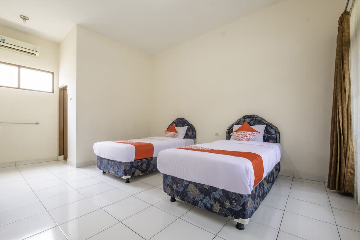 A hotel room with two beds, white bedding, and orange accents.