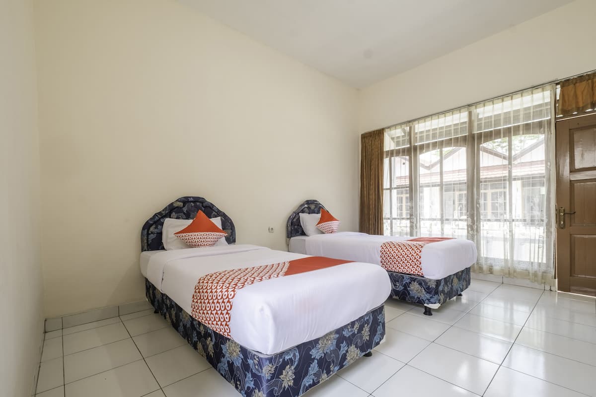 A hotel room with two beds, a large window with curtains, and a tiled floor.