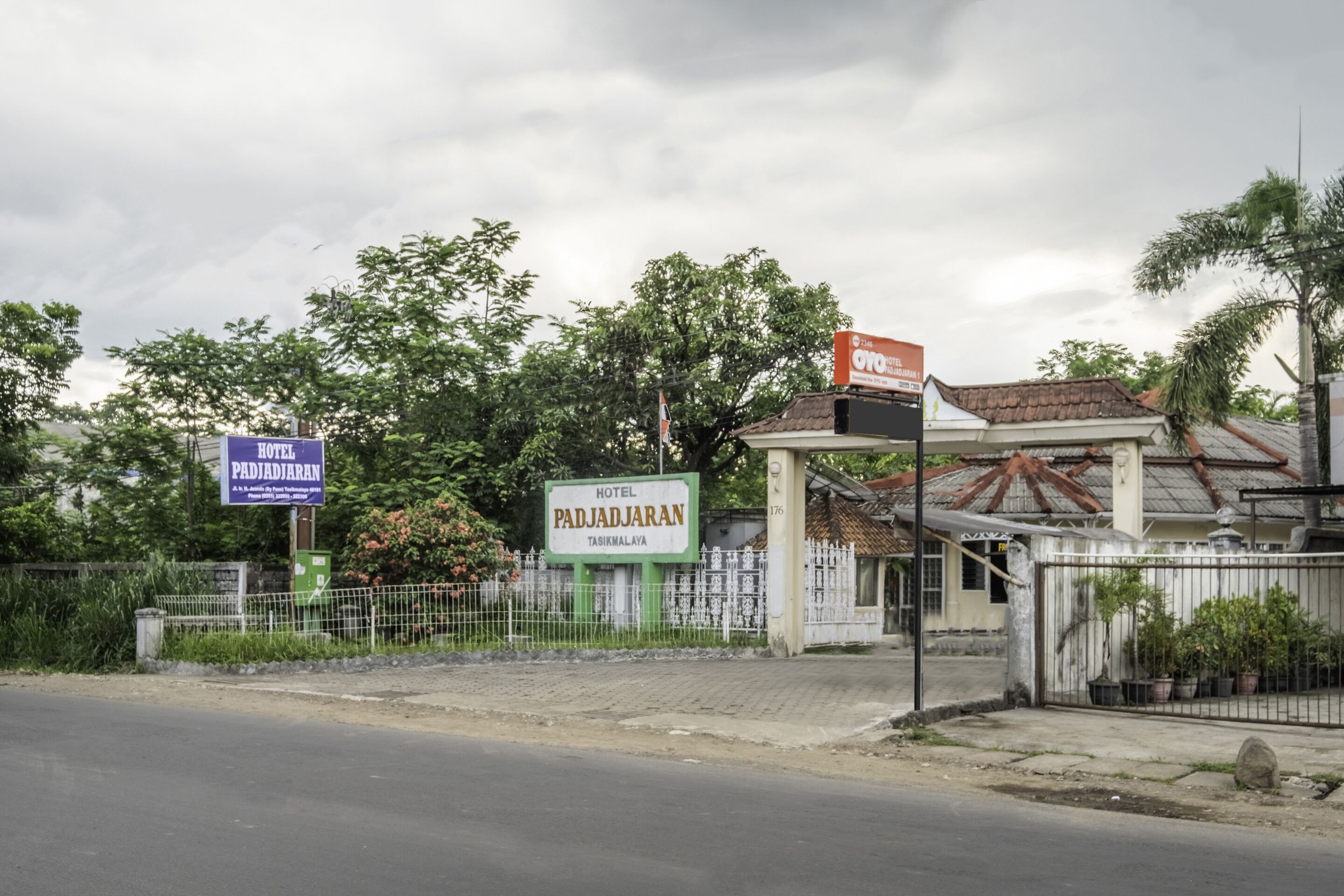 A hotel entrance with a signboard, a gated area, and a road in front.
